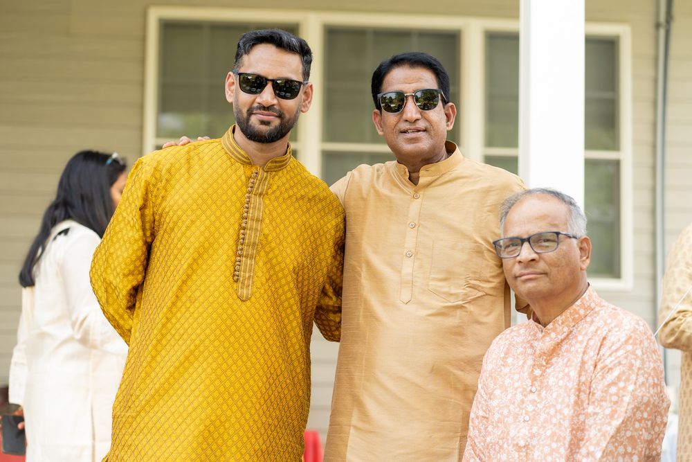 Group dressed in traditional Indian attire including yellow and orange kurtas gather together on a bright sunny day. Haldi Quad Cities Photo