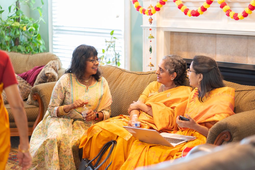 People in orange attire gather at a festive event with multiple seating areas and decorative elements. Haldi Quad Cities Photography