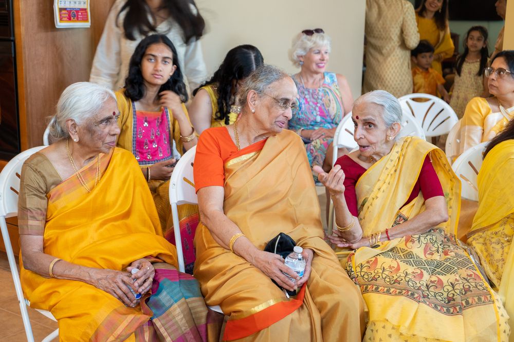 Group of women in traditional Indian attire seated together at a cultural gathering wearing yellow and orange saris. Haldi Quad Cities Photo