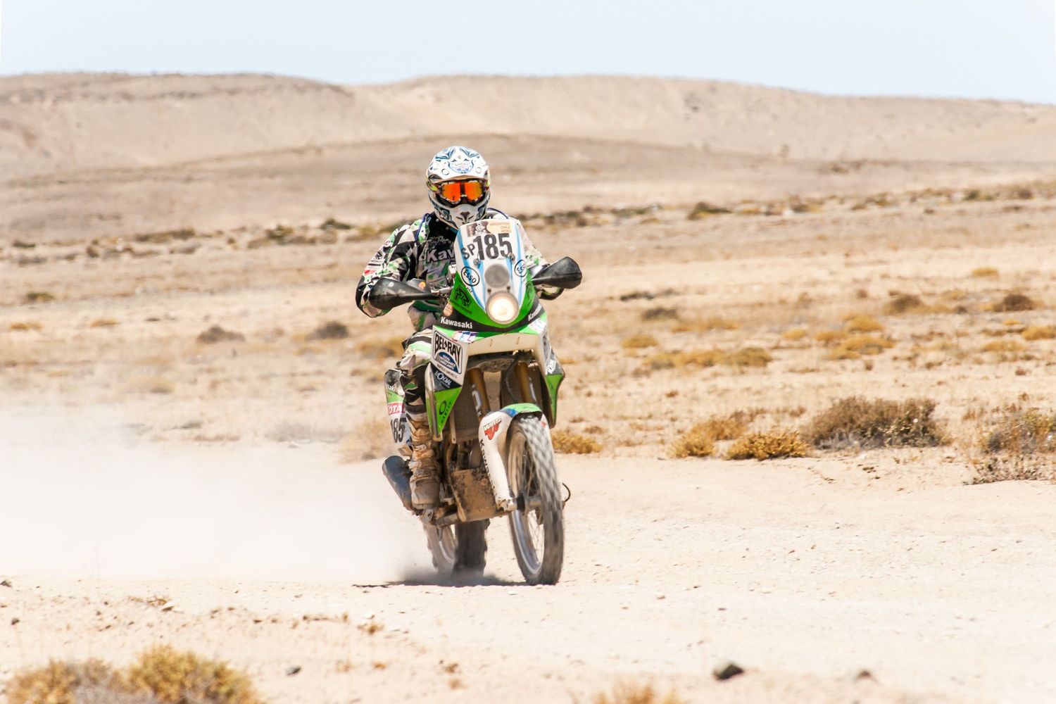 Rally car kicks up sand while racing through desert terrain during an off-road competition.