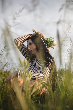 A person in striped clothing lies dreamily in tall wild grass during golden hour.