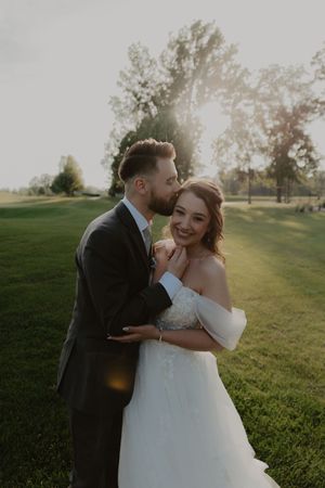 A romantic wedding couple shares candid moments together on a sunlit grassy hill at golden hour.