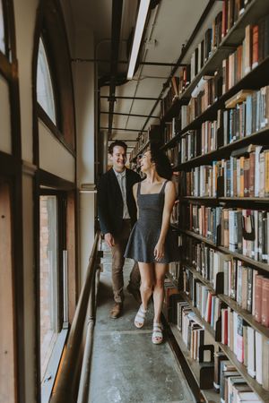 A couple in casual outfits sharing intimate moments while browsing books in a library's long corridors.