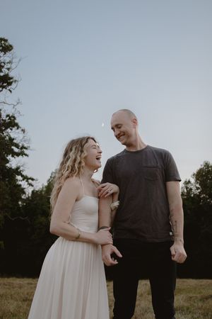 Two people share a candid moment together in an outdoor field during golden hour.