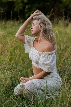 Ethereal portrait series of someone in a white eyelet dress lying gracefully in tall summer grass at golden hour.