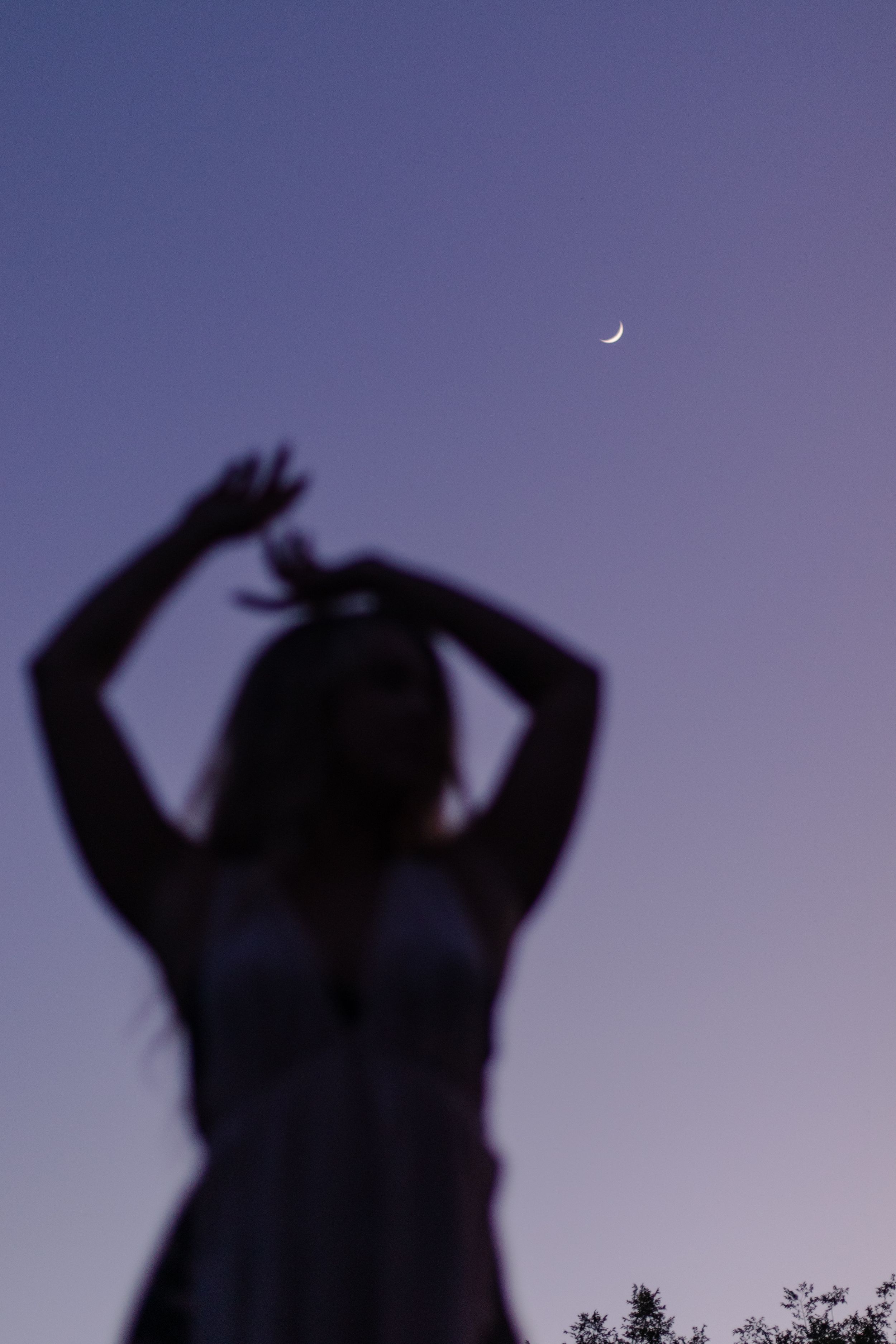 Silhouette of a person with raised arms at sunset against a dark blue sky.