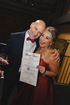 A couple in formal attire share joyful moments while holding a diploma or certificate at a graduation celebration.