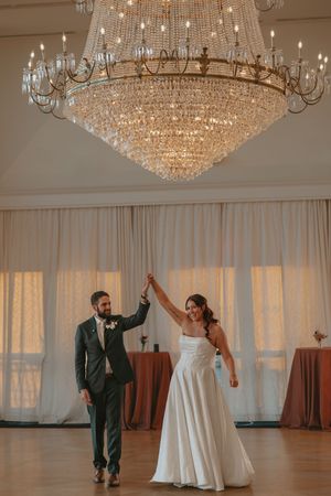 A couple dances together in an elegant ballroom under sparkling crystal chandeliers during their wedding celebration.