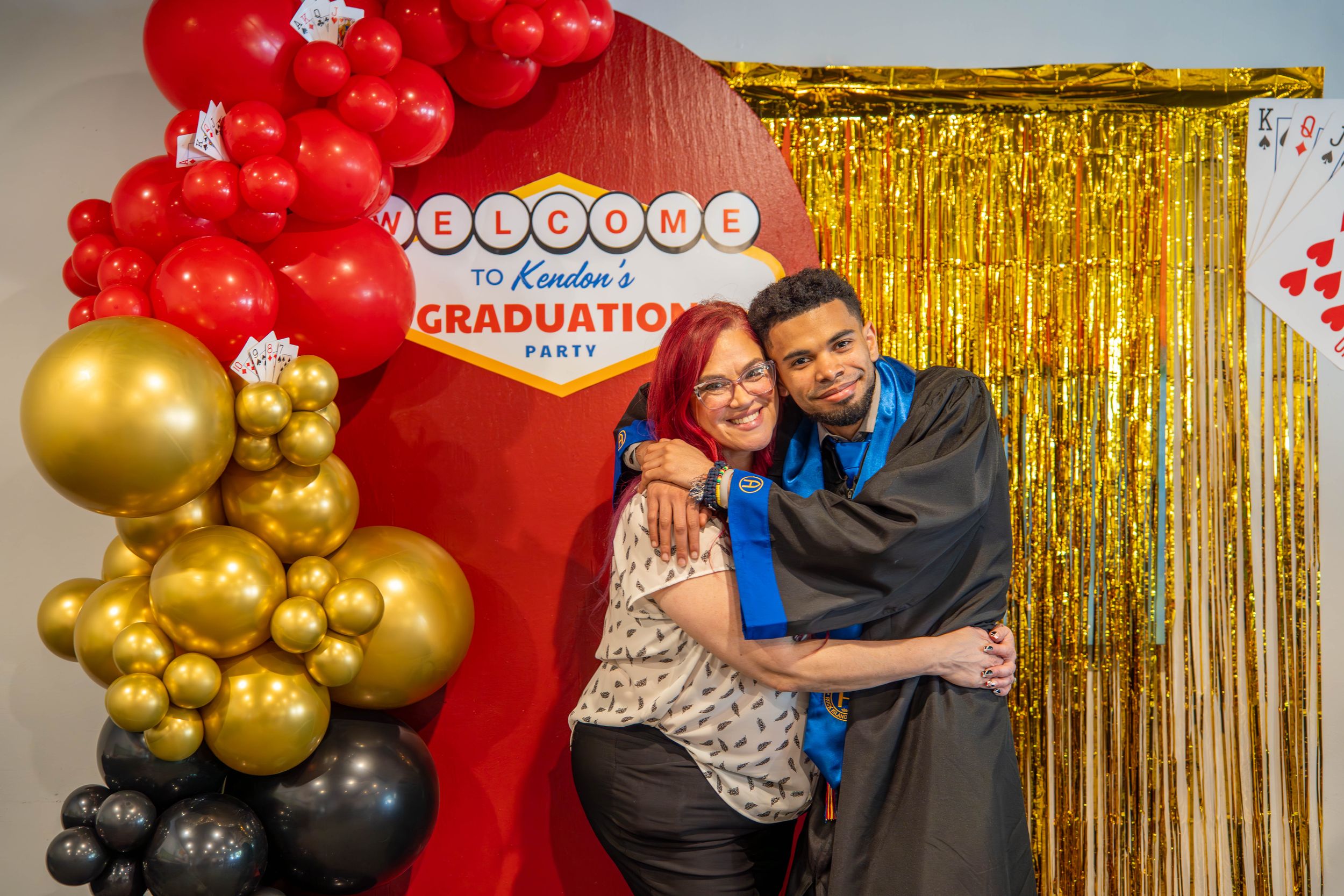 Festive red and gold balloon arch backdrop with gold tinsel curtain for graduation celebration photoshoot. Quad Cities Photography