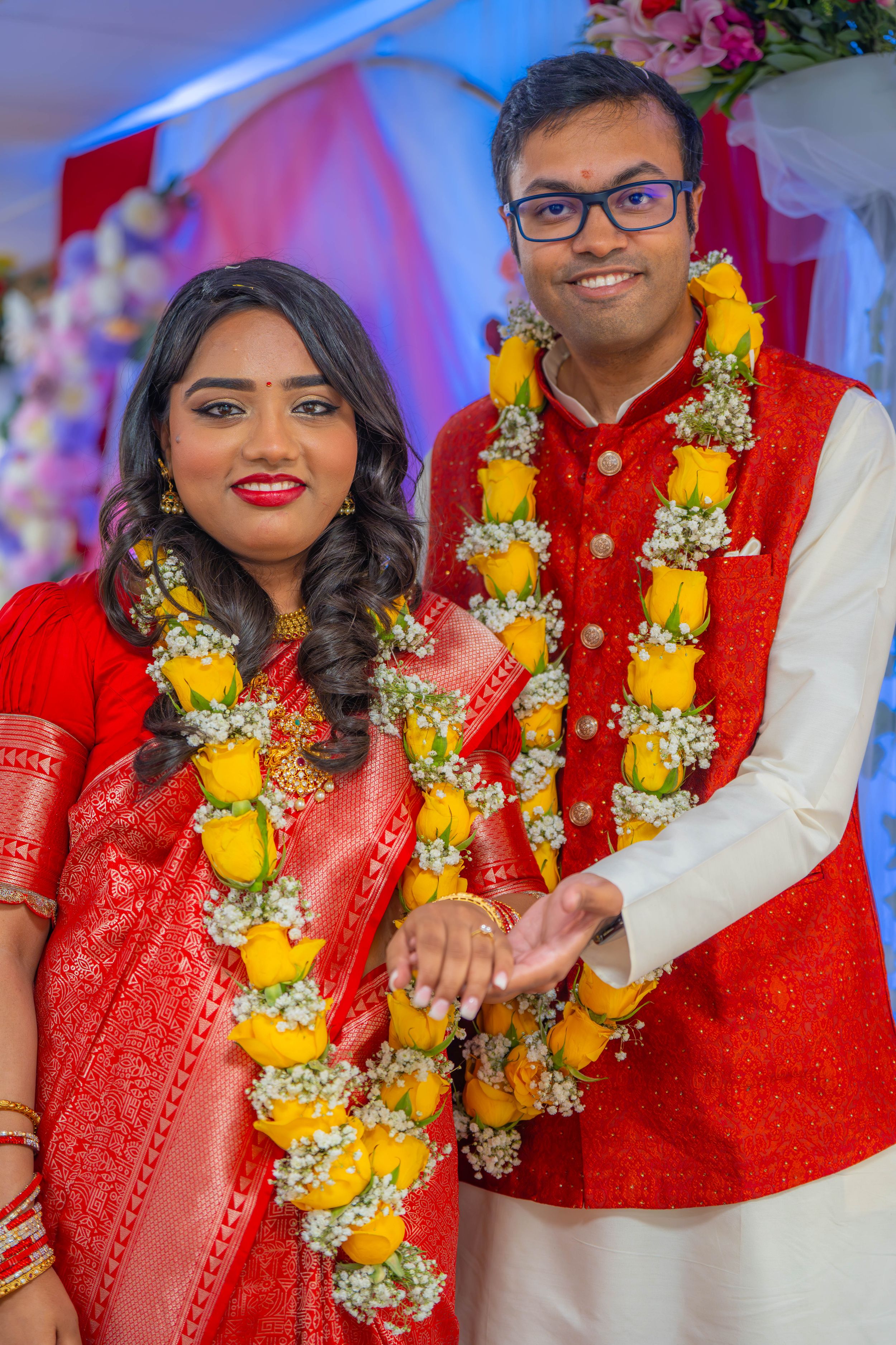 Traditional Indian couple wearing red wedding attire and yellow floral garlands during celebration ceremony. Quad Cities Photography