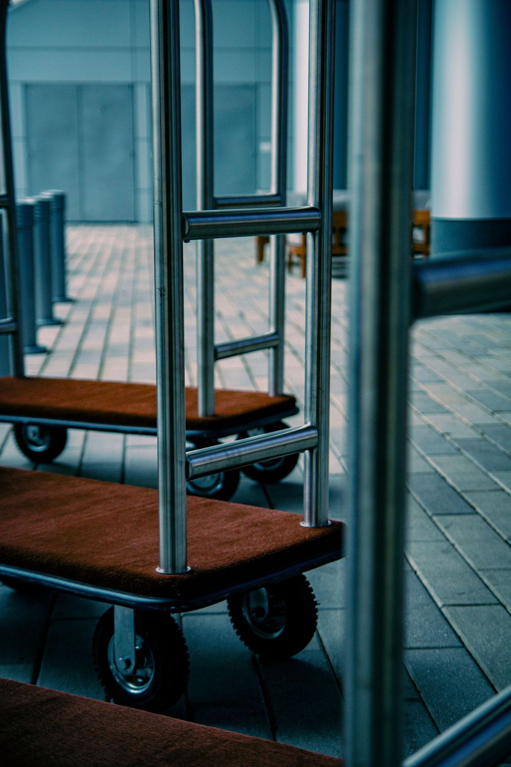 Metal luggage cart with wooden platform and wheels on tiled floor in indoor hallway setting.