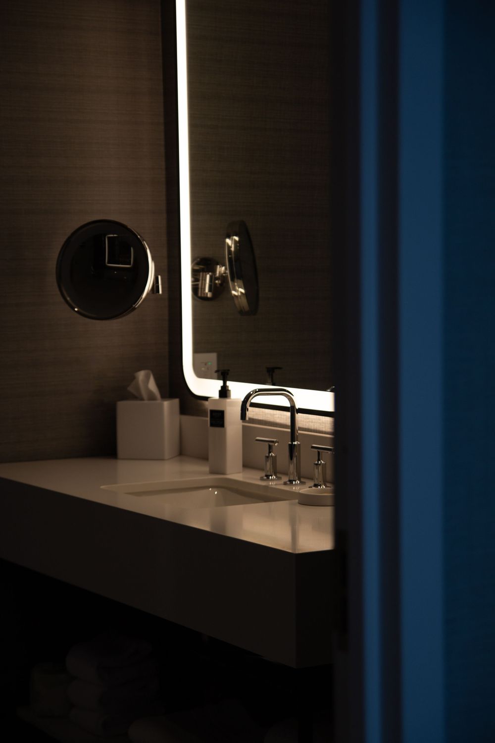 Modern bathroom features a sleek white countertop with dark walls and minimalist lighting fixtures in moody ambiance.