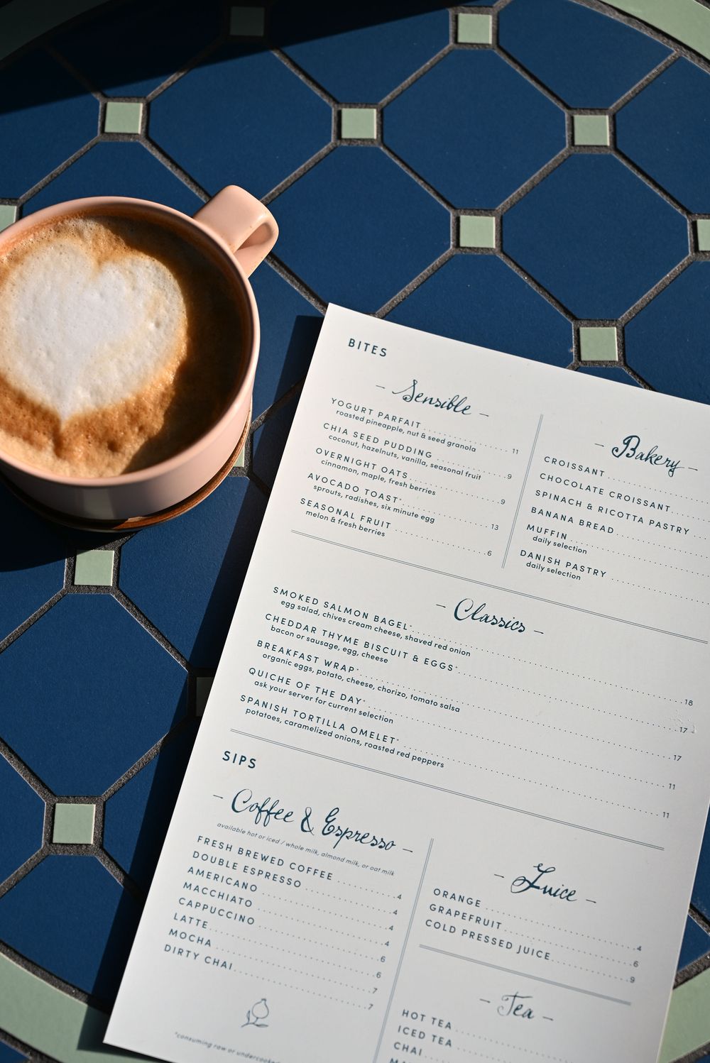 A coffee cup with latte art sits beside a restaurant menu on a blue geometric patterned table.