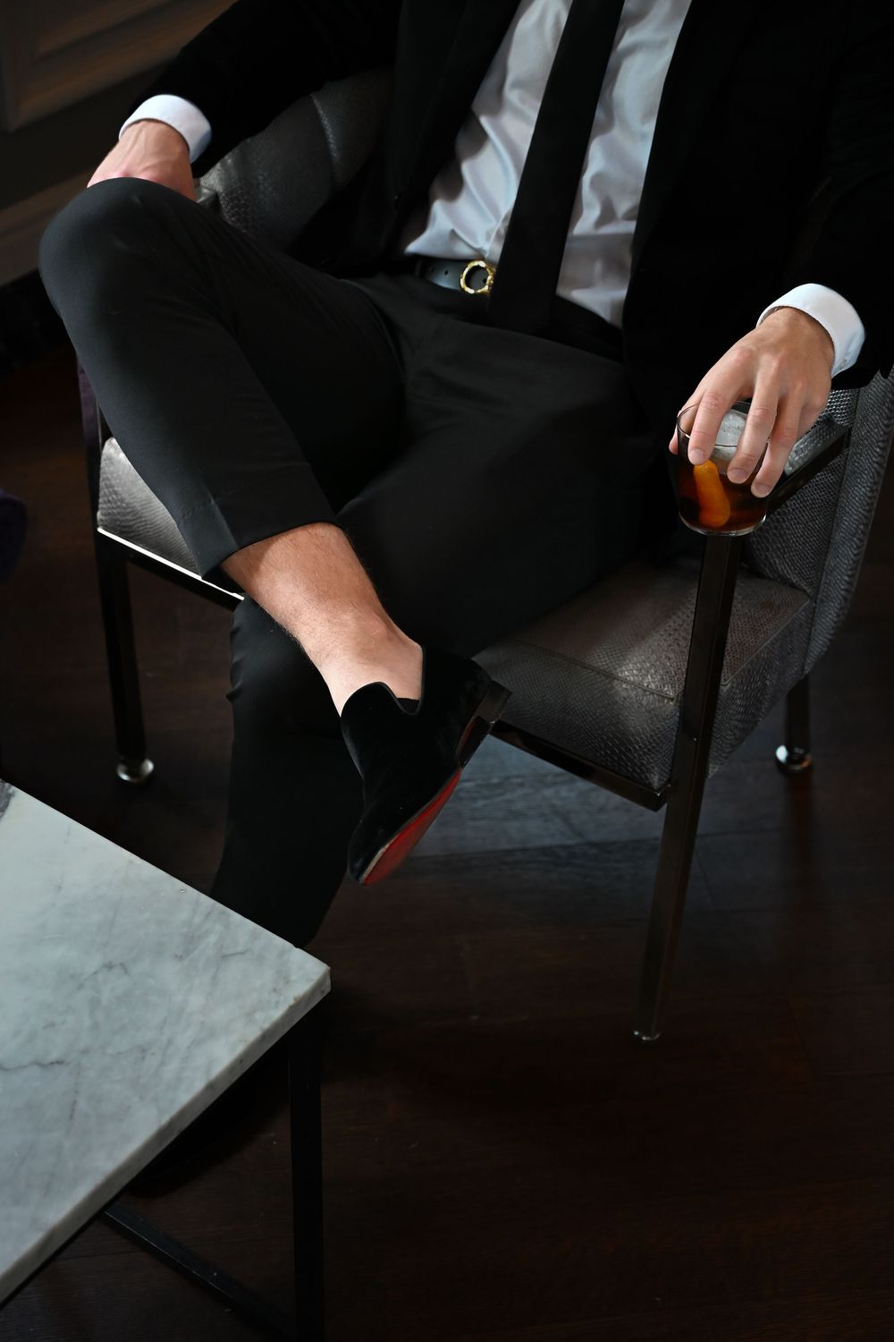 Close-up shot of a person in formal business attire seated on a dark leather chair with a drink.