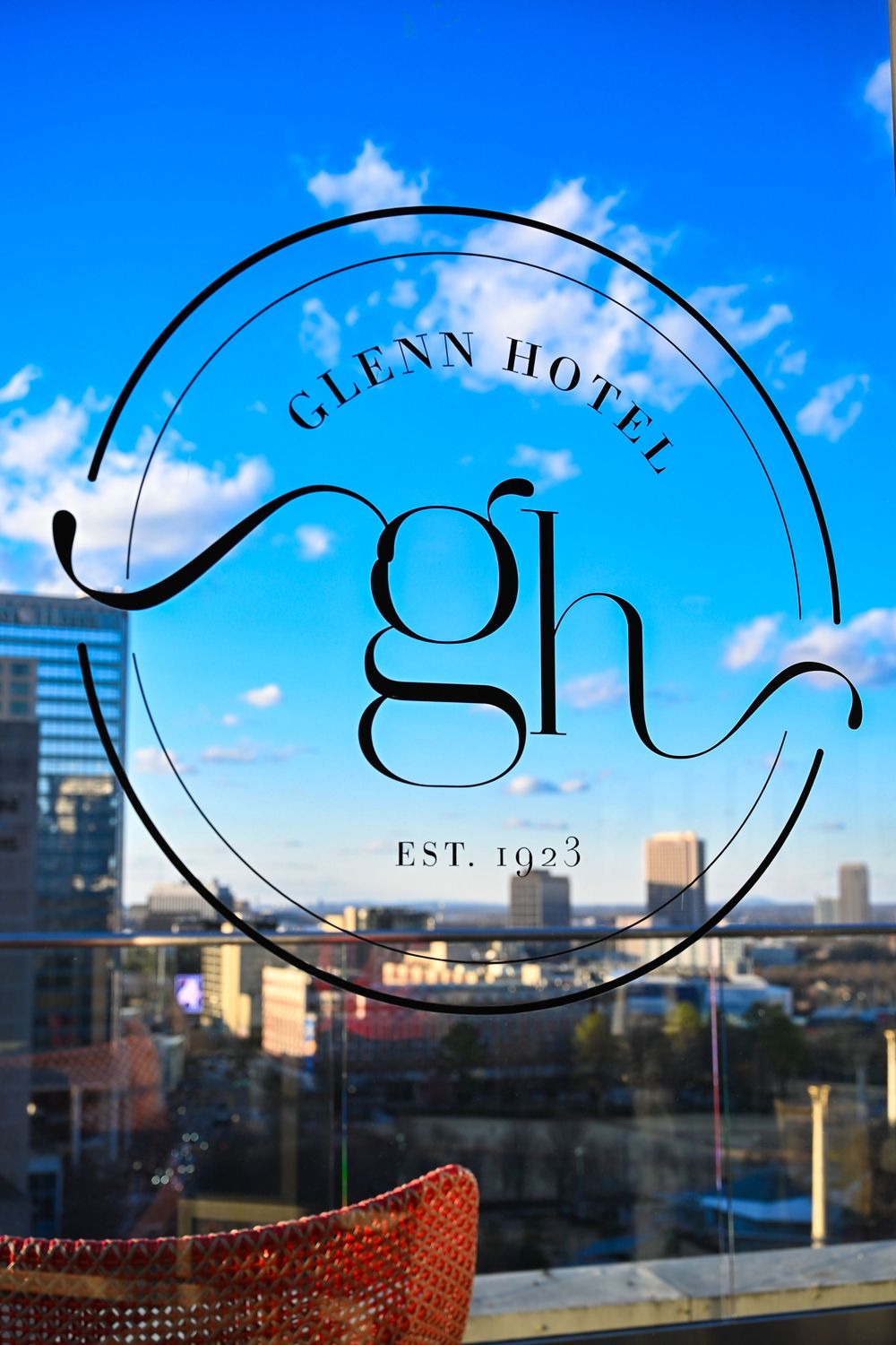 Glenn Hotel est. 1923 logo on glass with Atlanta skyline and blue sky in background.
