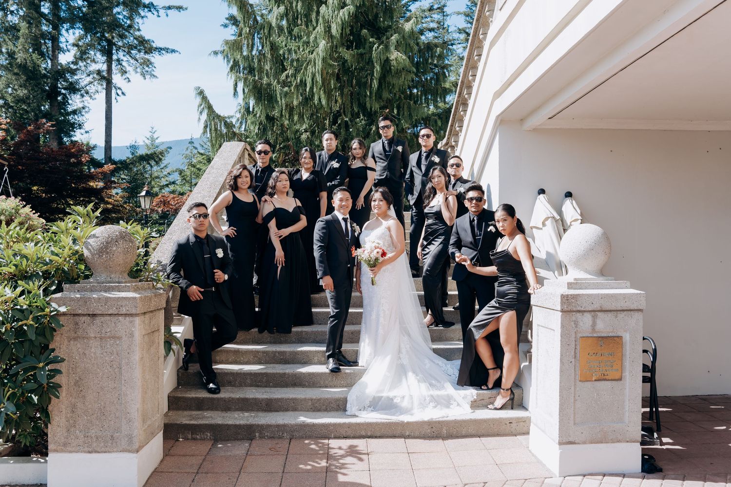 A wedding party in formal attire poses on grand outdoor stone steps.