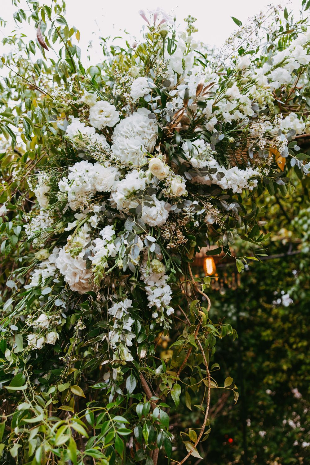 White floral arrangements with greenery create an elegant wedding arch decoration against a natural outdoor backdrop.