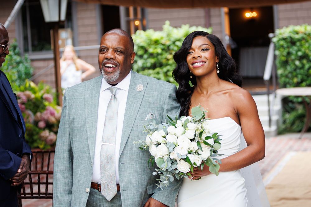A joyful couple shares laughter and embraces during their outdoor wedding celebration with white floral bouquets.