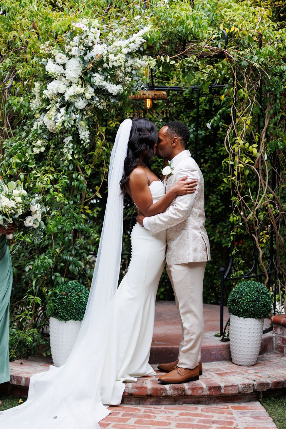 A romantic wedding ceremony under a floral arch with white roses and greenery in a garden setting at the Chapel of Orange in Orange County.