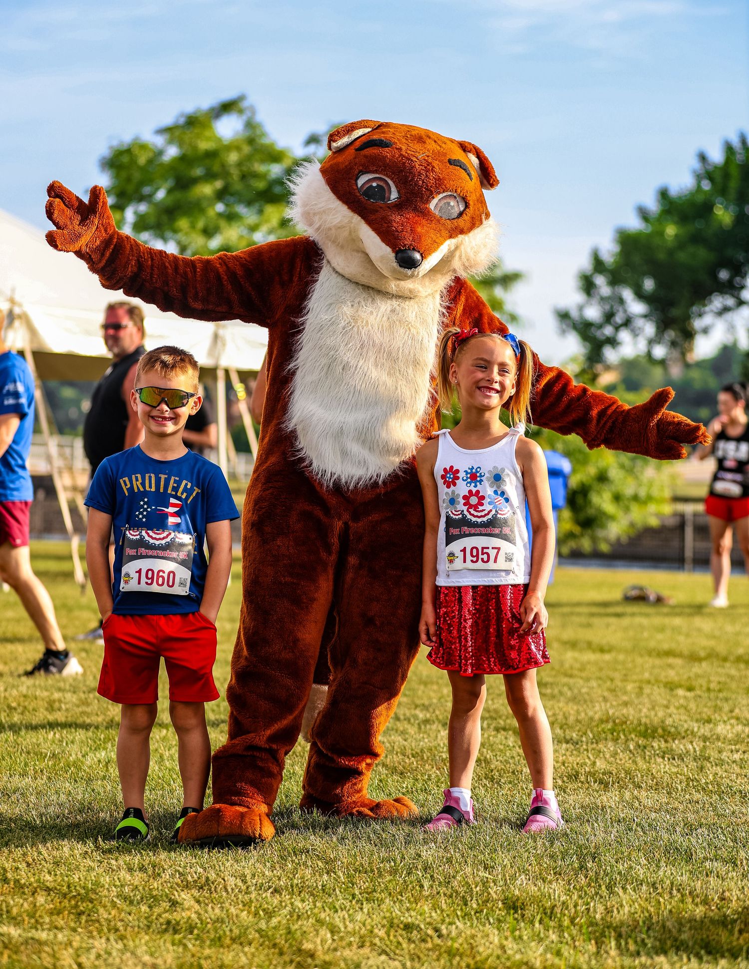 Brown mascot bear character interacting with participants at an outdoor summer sporting event.