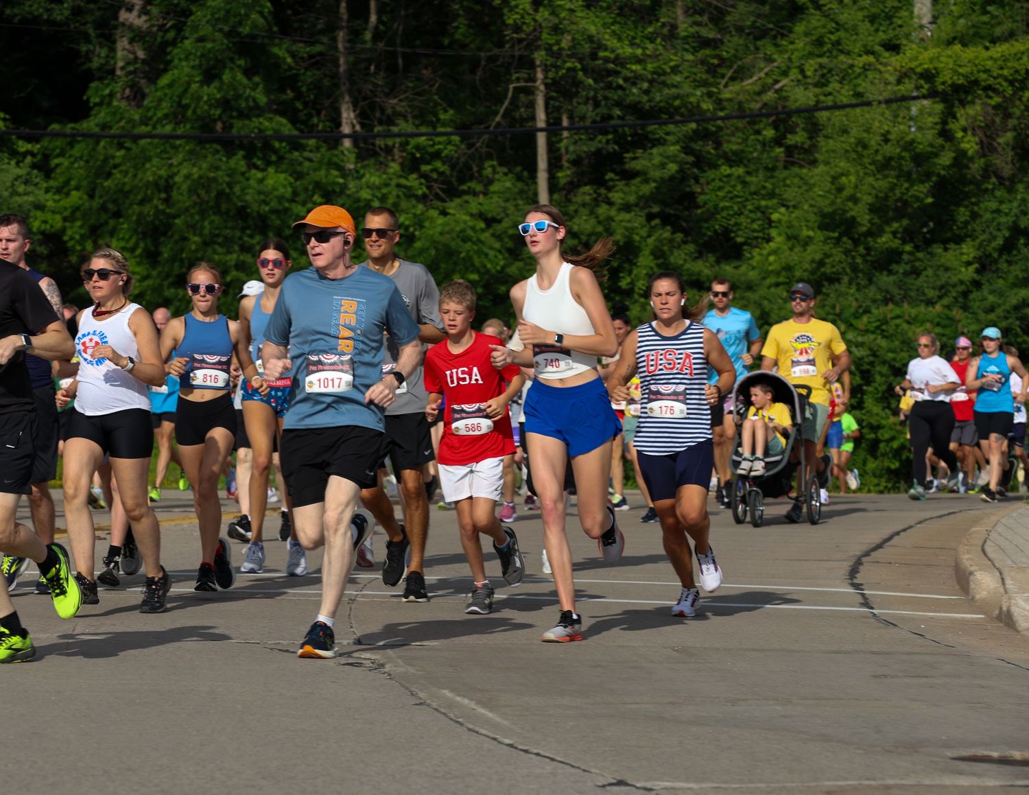 Runners participating in a race along a tree-lined path on a sunny summer day.