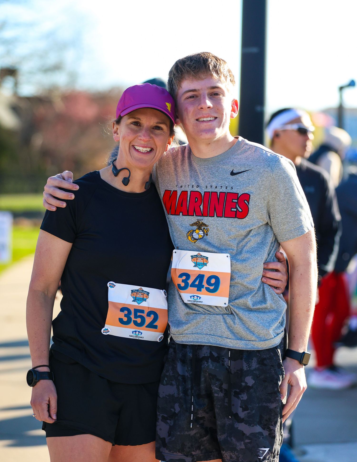 Two runners wearing race bibs 352 and 349 pose together at an outdoor 5K race event on a sunny day.