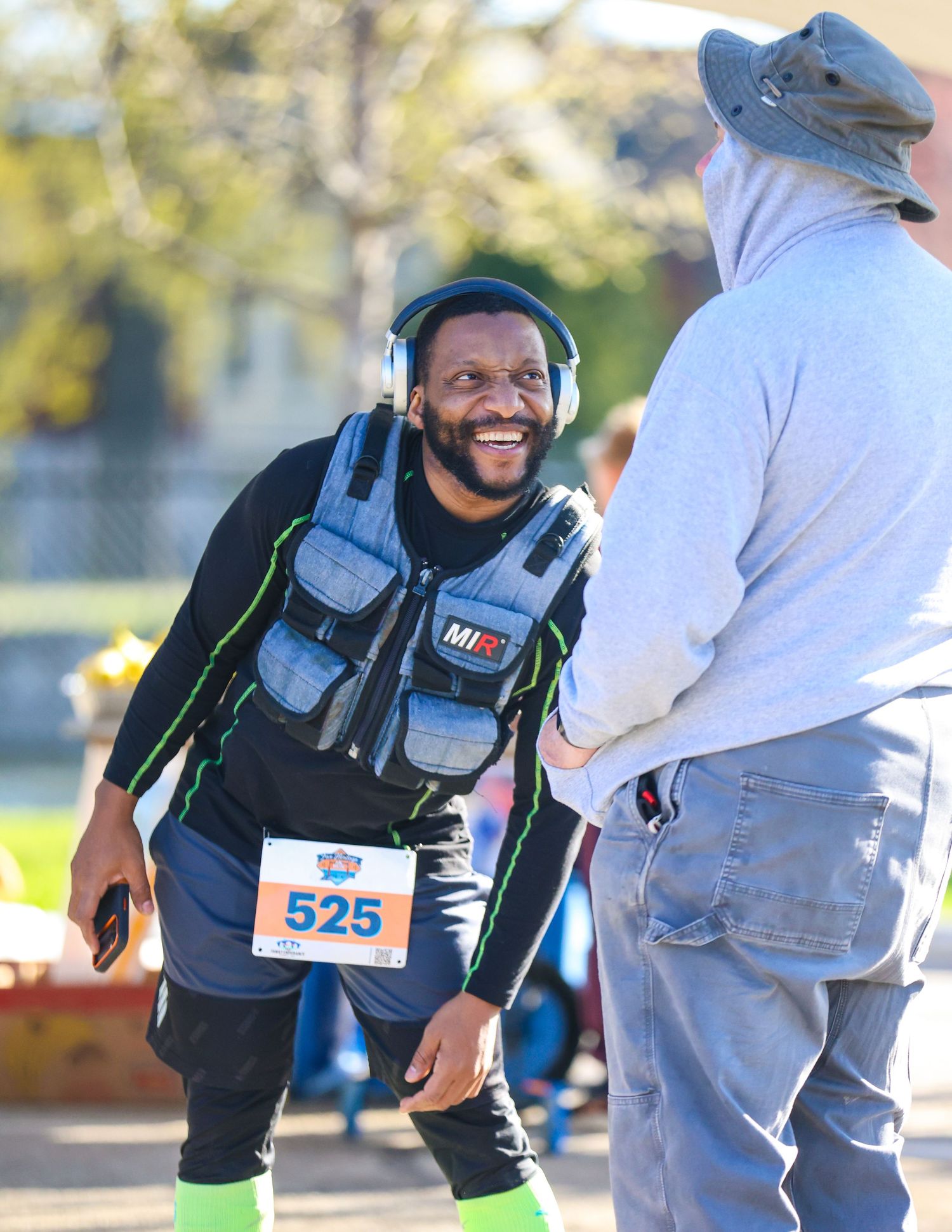 Smiling male runner wearing bib number 525 and headphones at an outdoor race event.