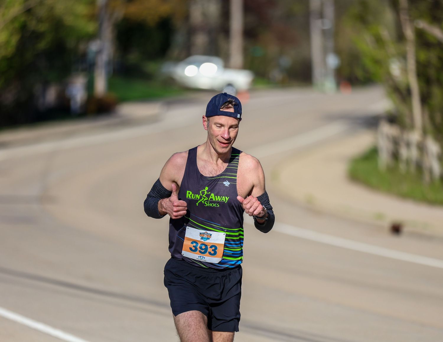 Runner wearing bib number 393 competing in an outdoor road race on a tree-lined street on a sunny day.