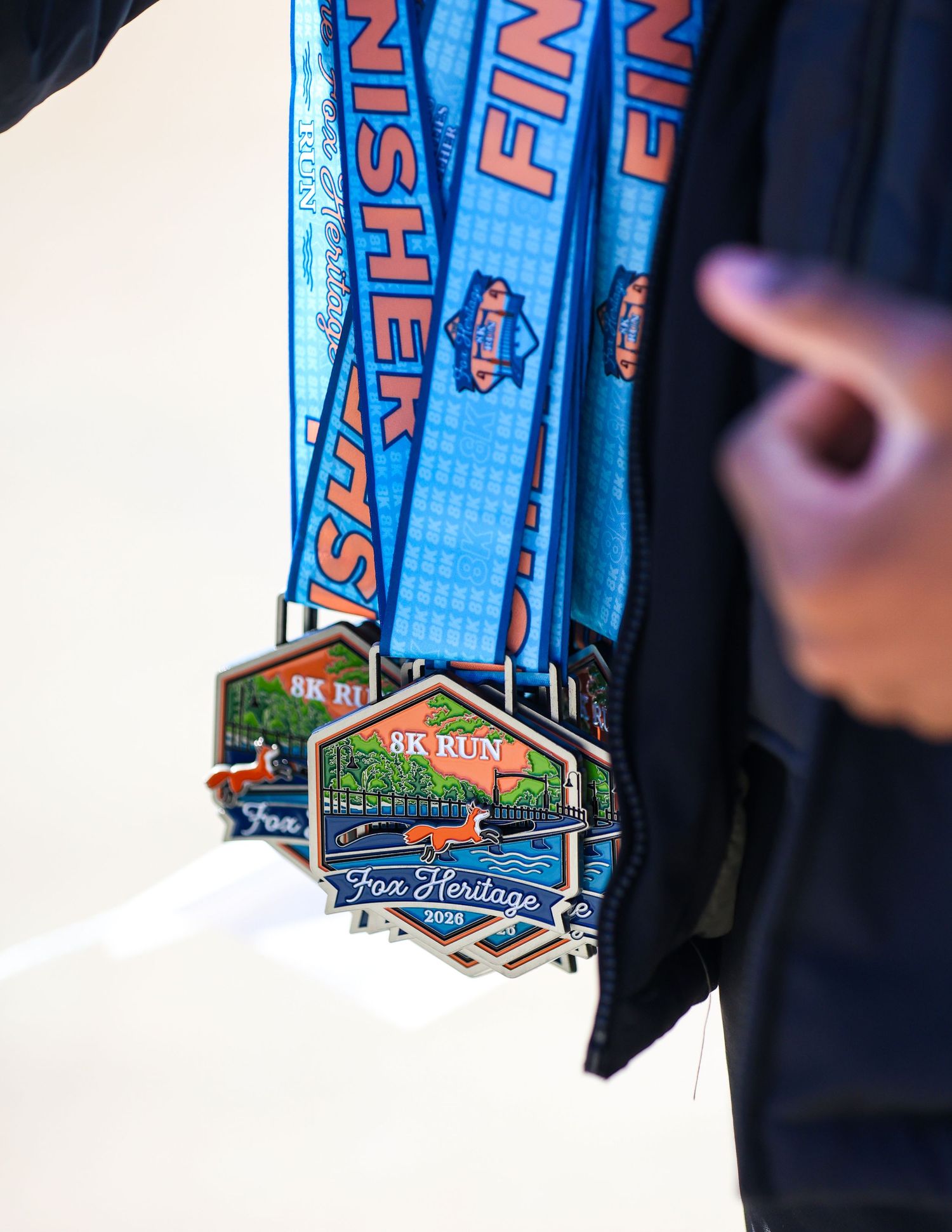 Fox Heritage 5K run finisher medals hanging on blue ribbons, awarded to race participants at a running event.