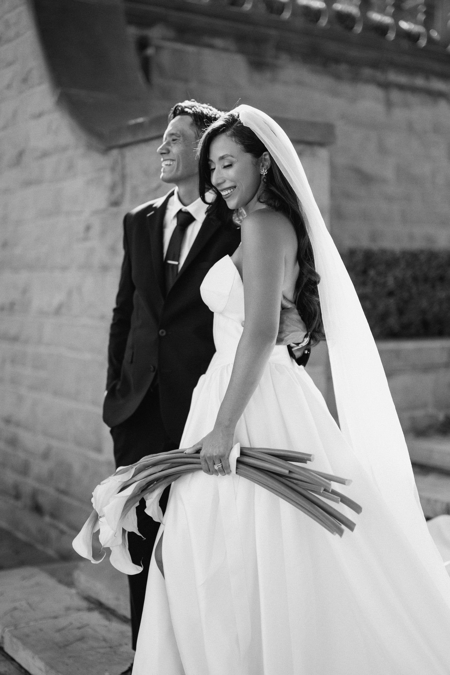 Black and white wedding photograph series showing a bride and groom walking along a stone wall.