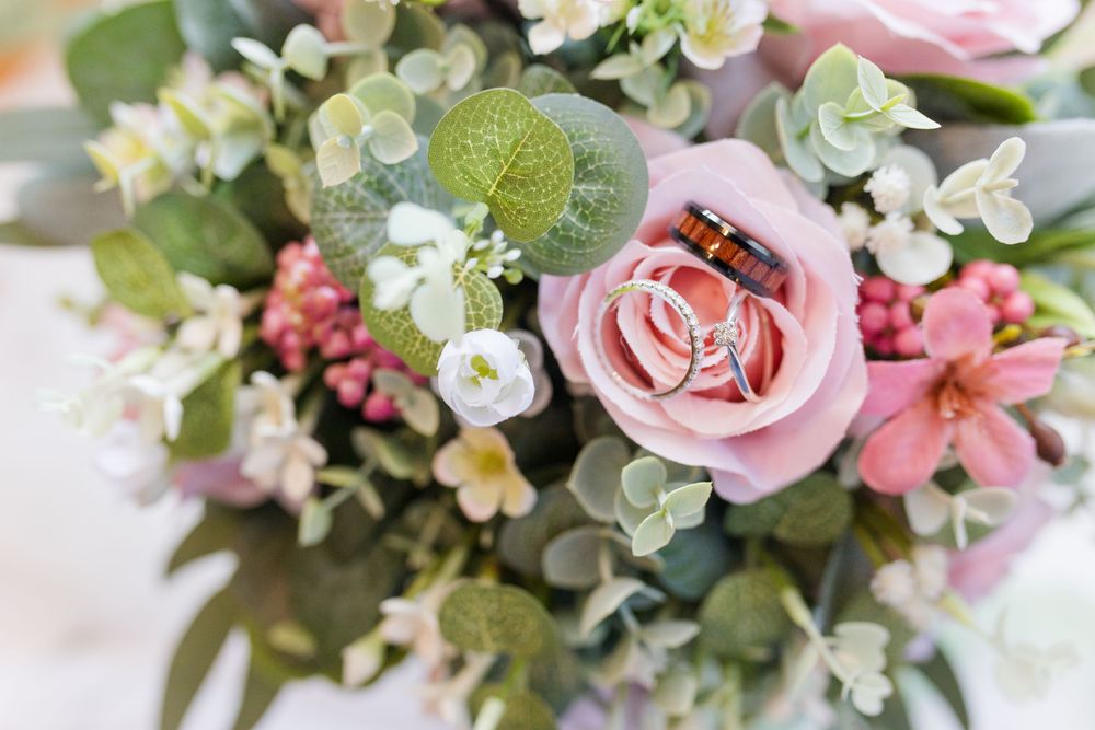 Close-up of a delicate pink rose and white blooms mixed with eucalyptus greenery in a romantic floral arrangement.