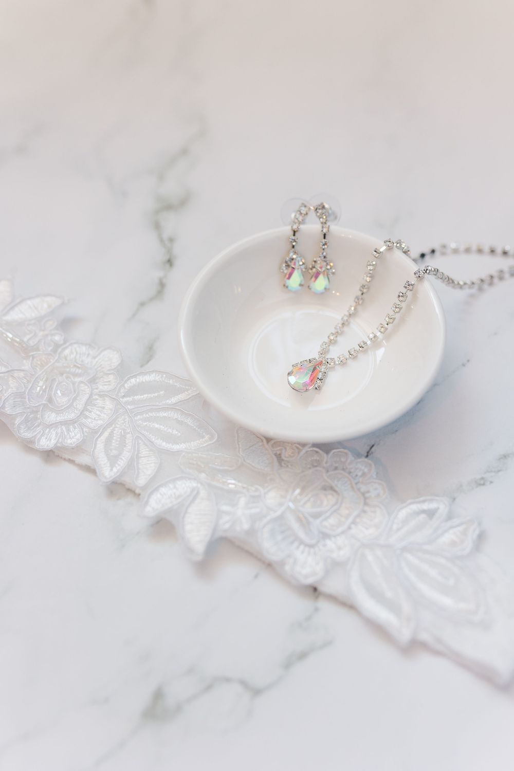 Delicate pearl earrings and white lace accessories displayed on a marble surface for a bridal photoshoot.