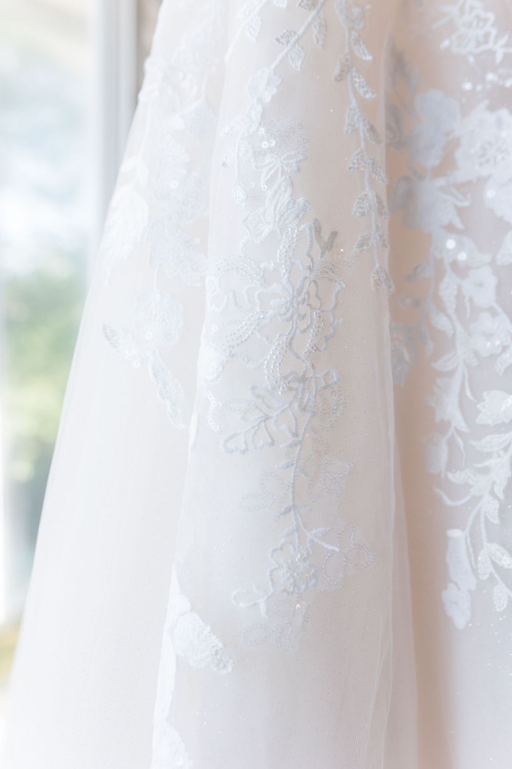 Close-up detail of delicate white lace and floral embroidery on wedding dress fabric.