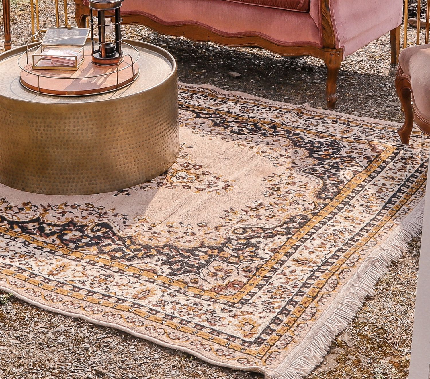 A vintage style ornate area rug with beige and brown tones lies beneath a brass drum coffee table and sofa.