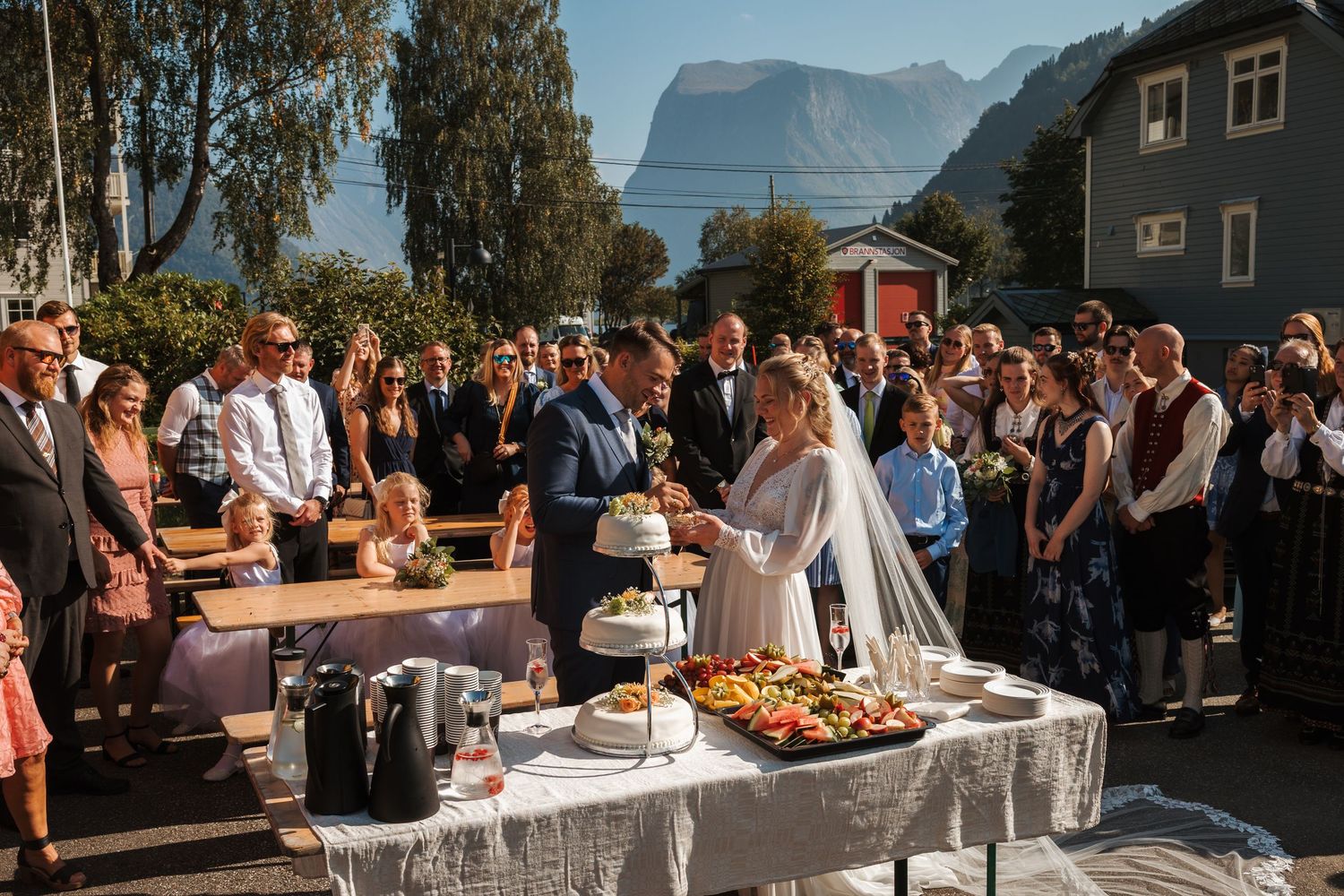 Outdoor wedding reception buffet table set against stunning Norwegian fjord and mountain landscape on sunny day.