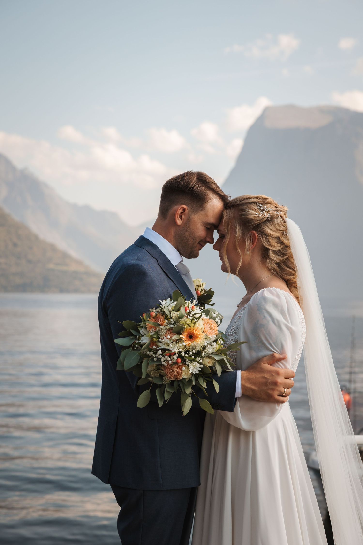 Couple shares intimate moment during lakeside wedding with mountains and water in the background.