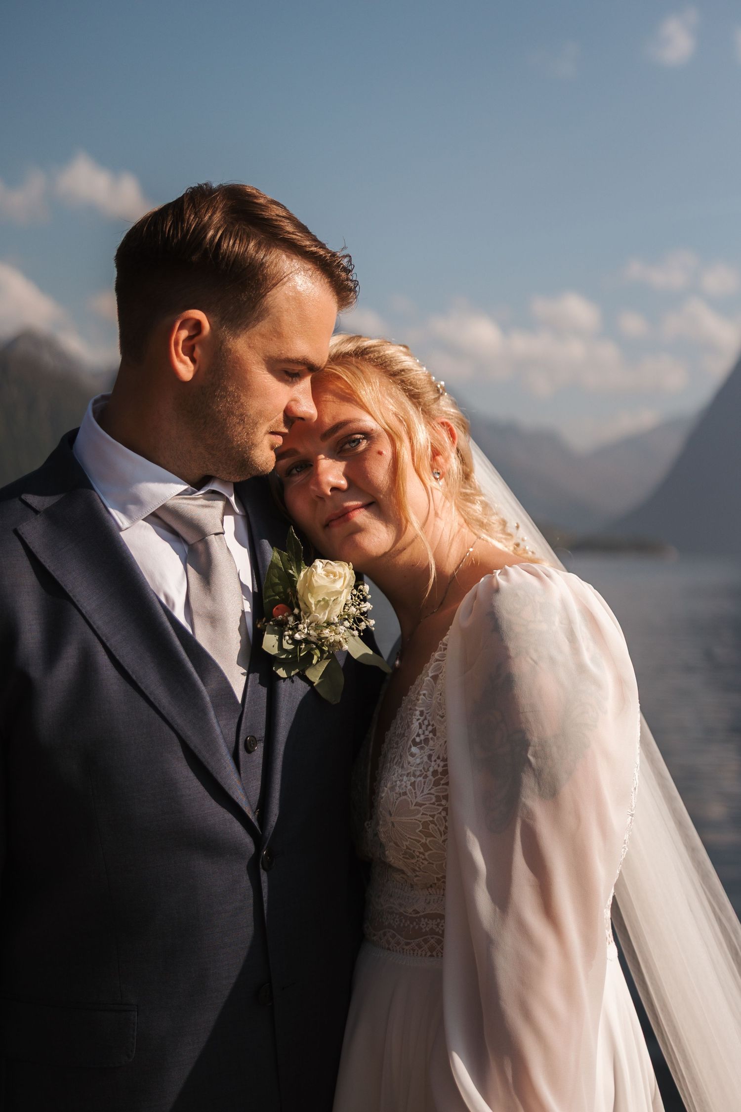 A romantic newlywed couple shares an intimate moment against a mountain landscape backdrop on their wedding day.