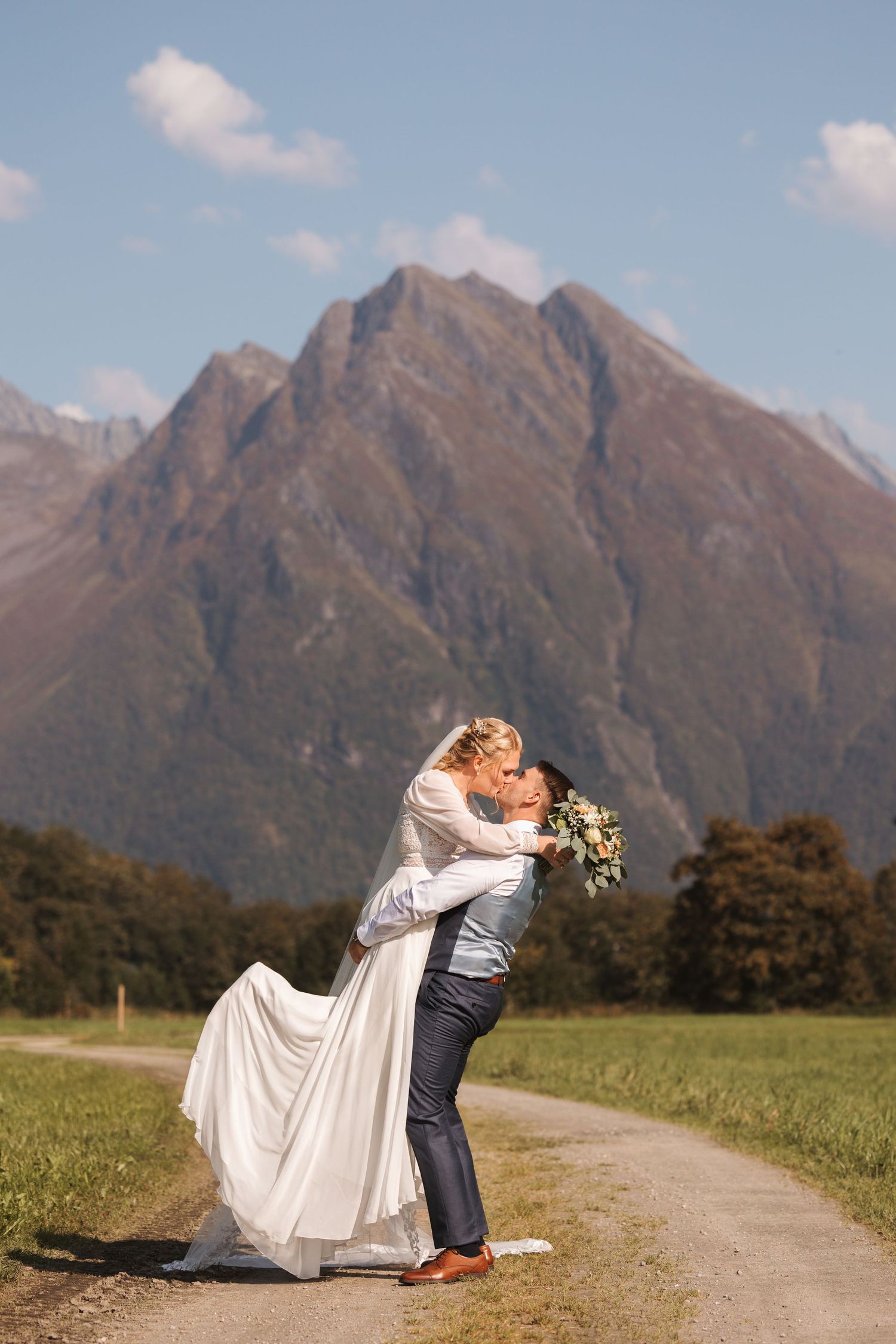 A romantic sequence of lovers embracing on a dirt road with majestic mountain peaks rising in the background.