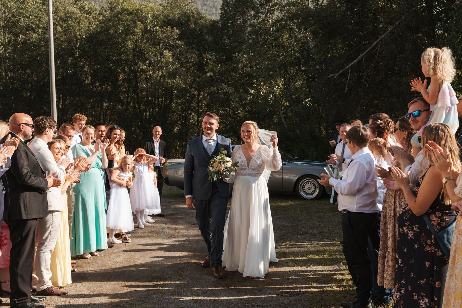A panoramic view of wedding guests gathered outdoors in a natural setting during a summer celebration.