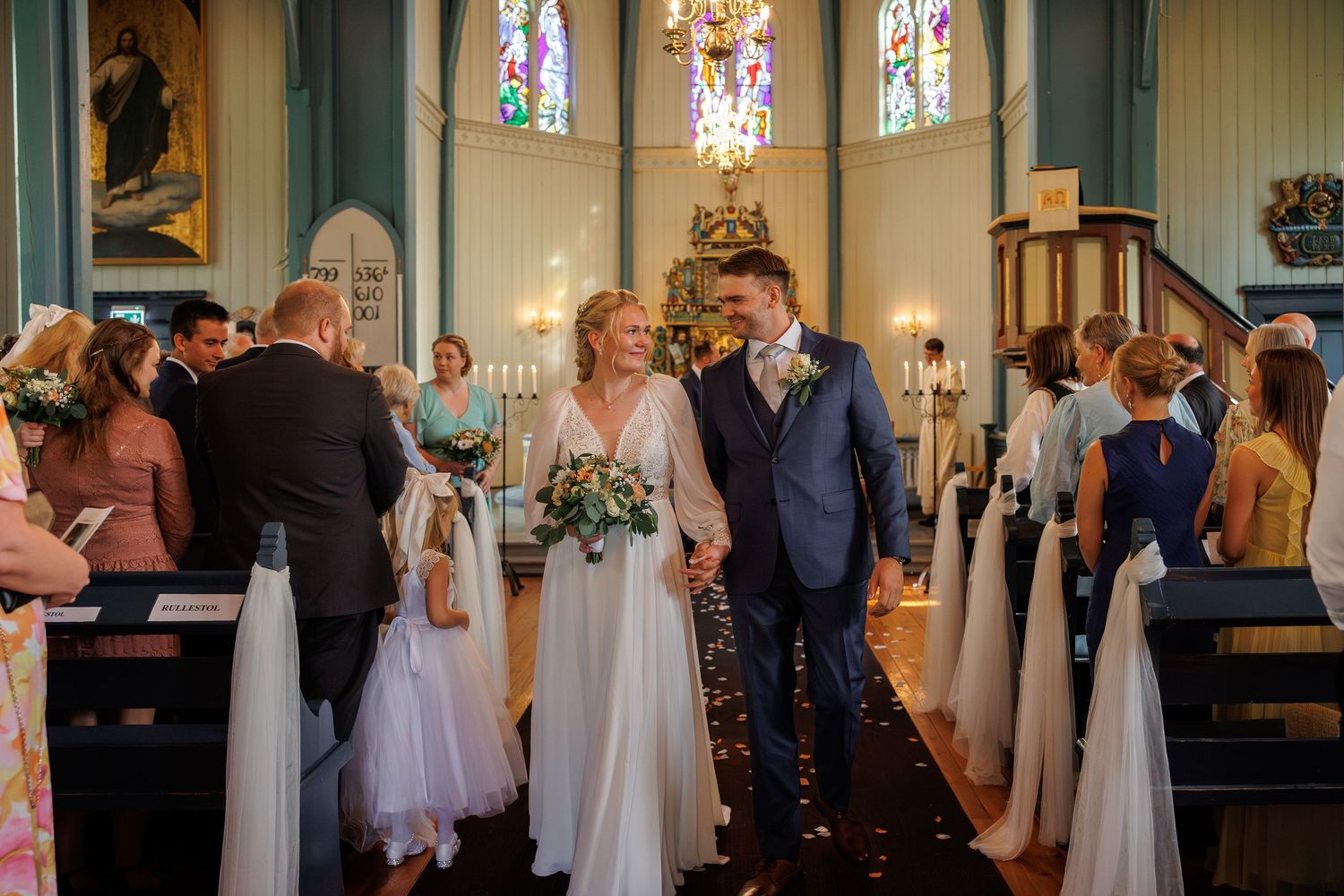 Wedding ceremony in a beautiful church sanctuary with stained glass windows and elegant chandeliers.