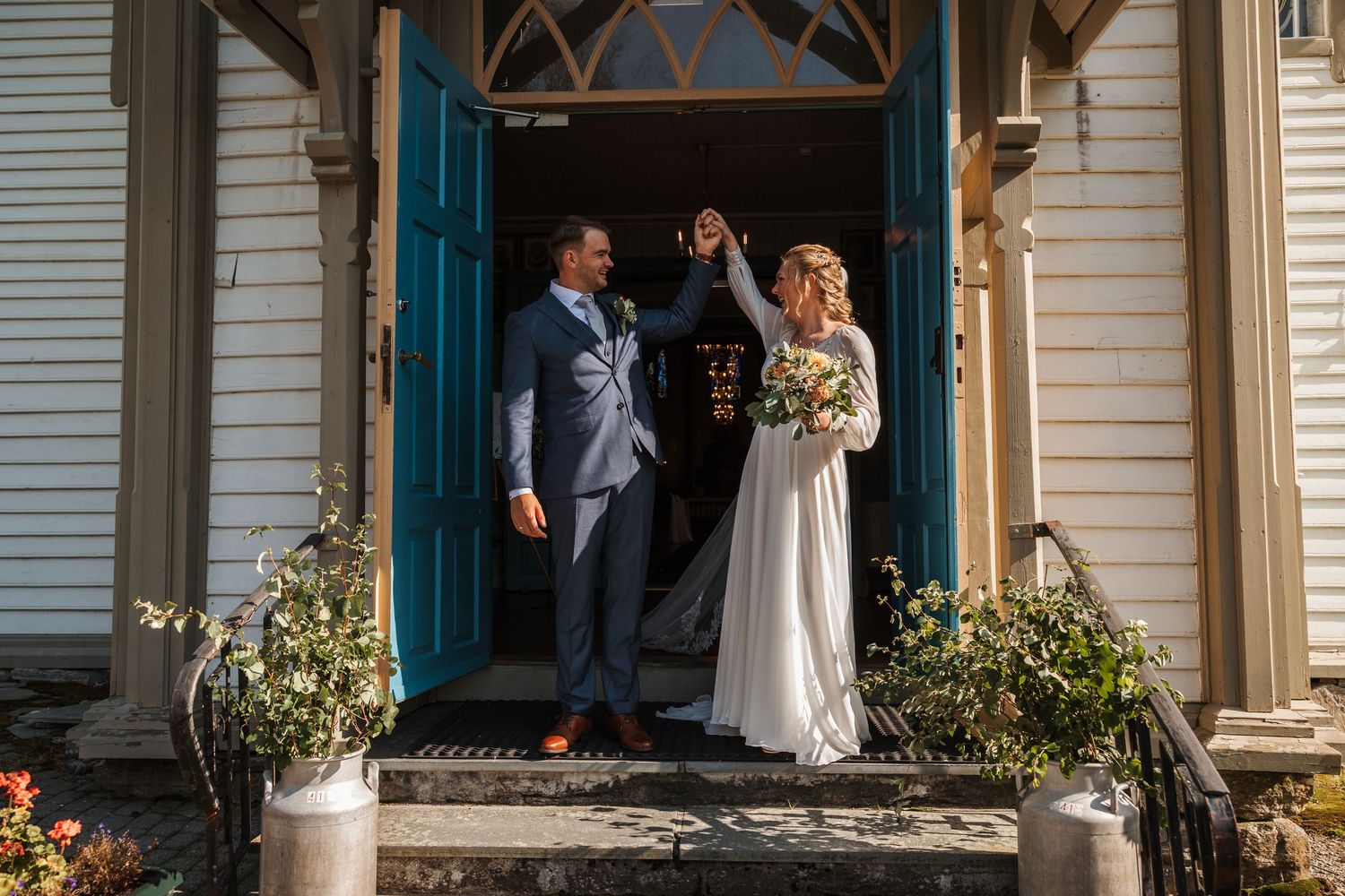 Bride and groom stand beneath rustic white Victorian porch archway during their outdoor wedding ceremony.