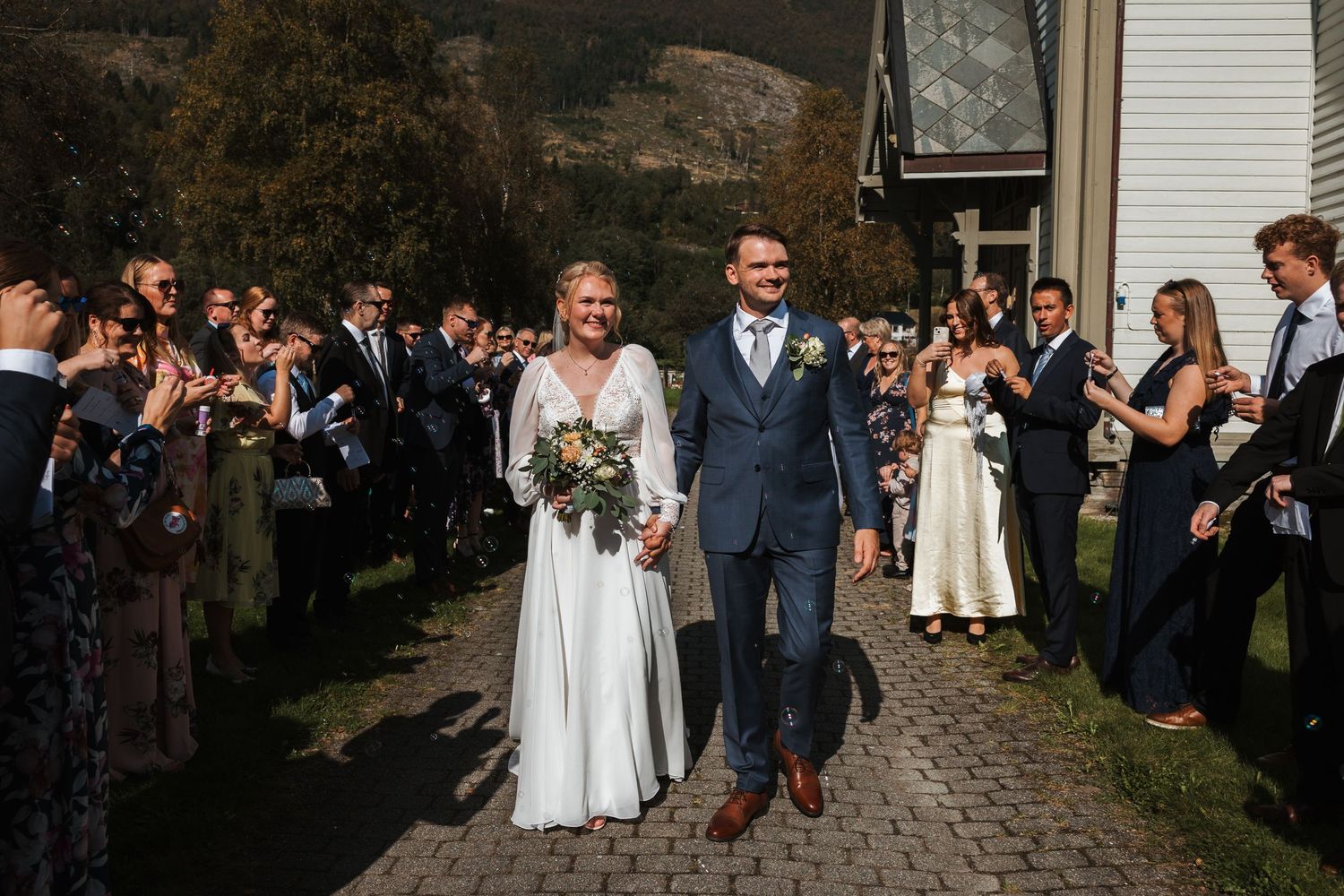 Wedding guests line a stone pathway to celebrate the newlyweds during an outdoor autumn ceremony.