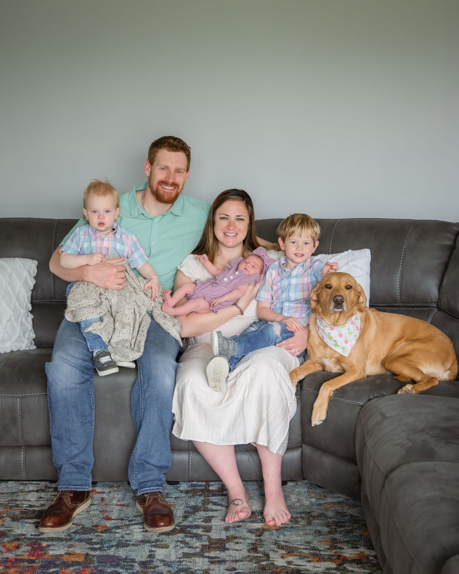 A family sits together on a gray sectional couch with their brown dog, creating a cozy home portrait.