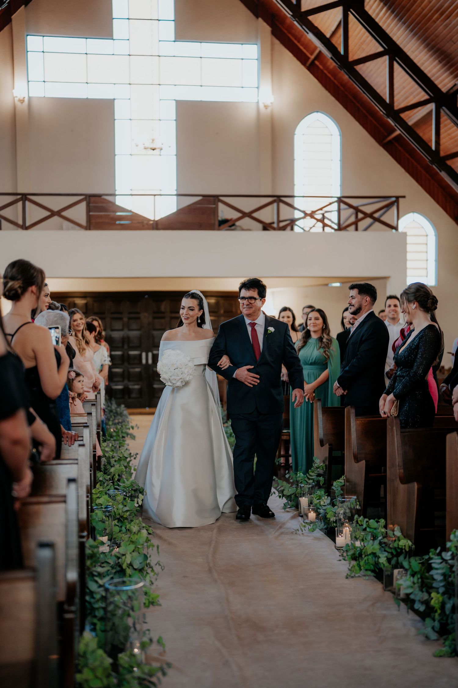 Wedding ceremony space with exposed wooden beams and greenery-lined aisle.