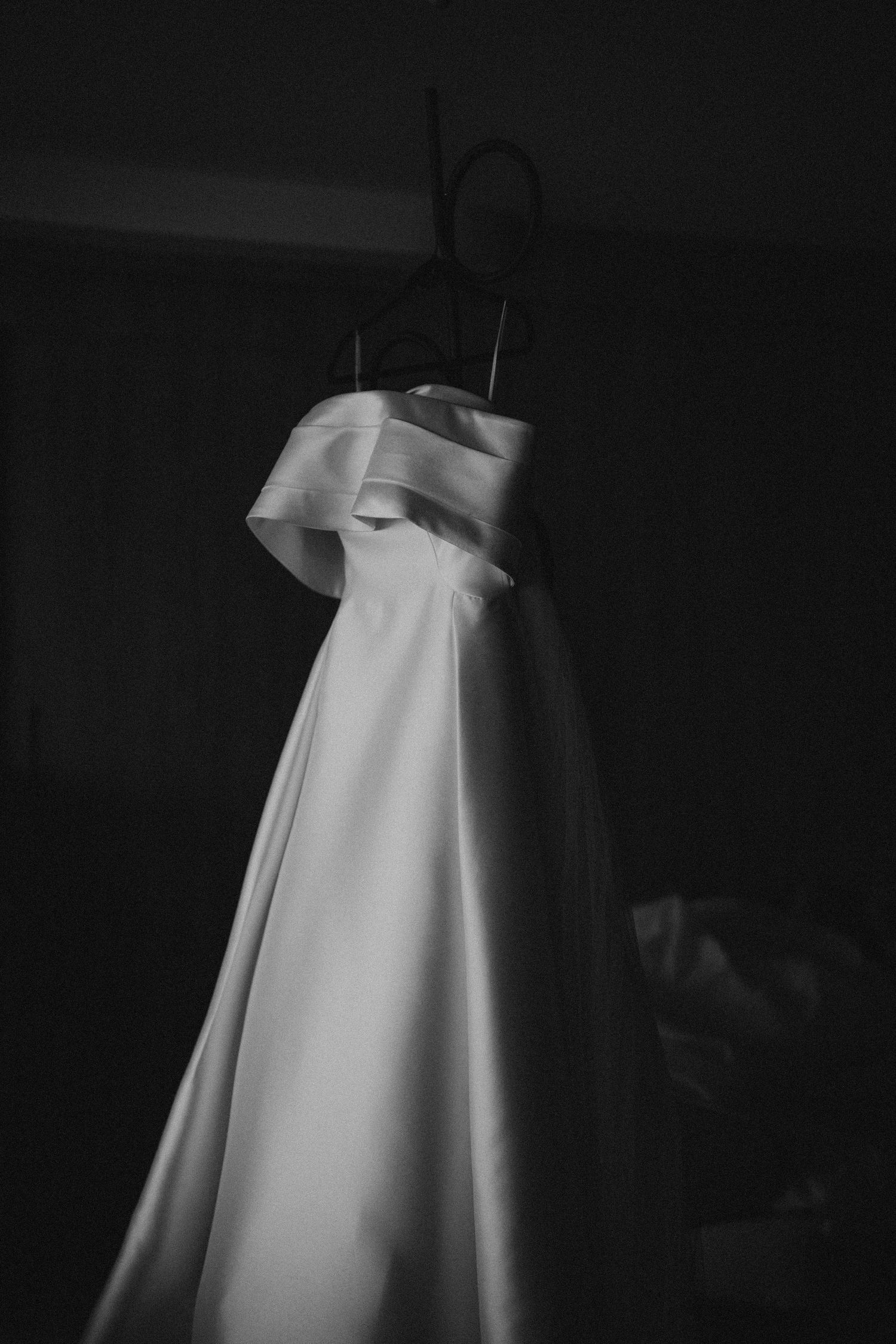 Classic white wedding gown hangs in dramatic black and white lighting.