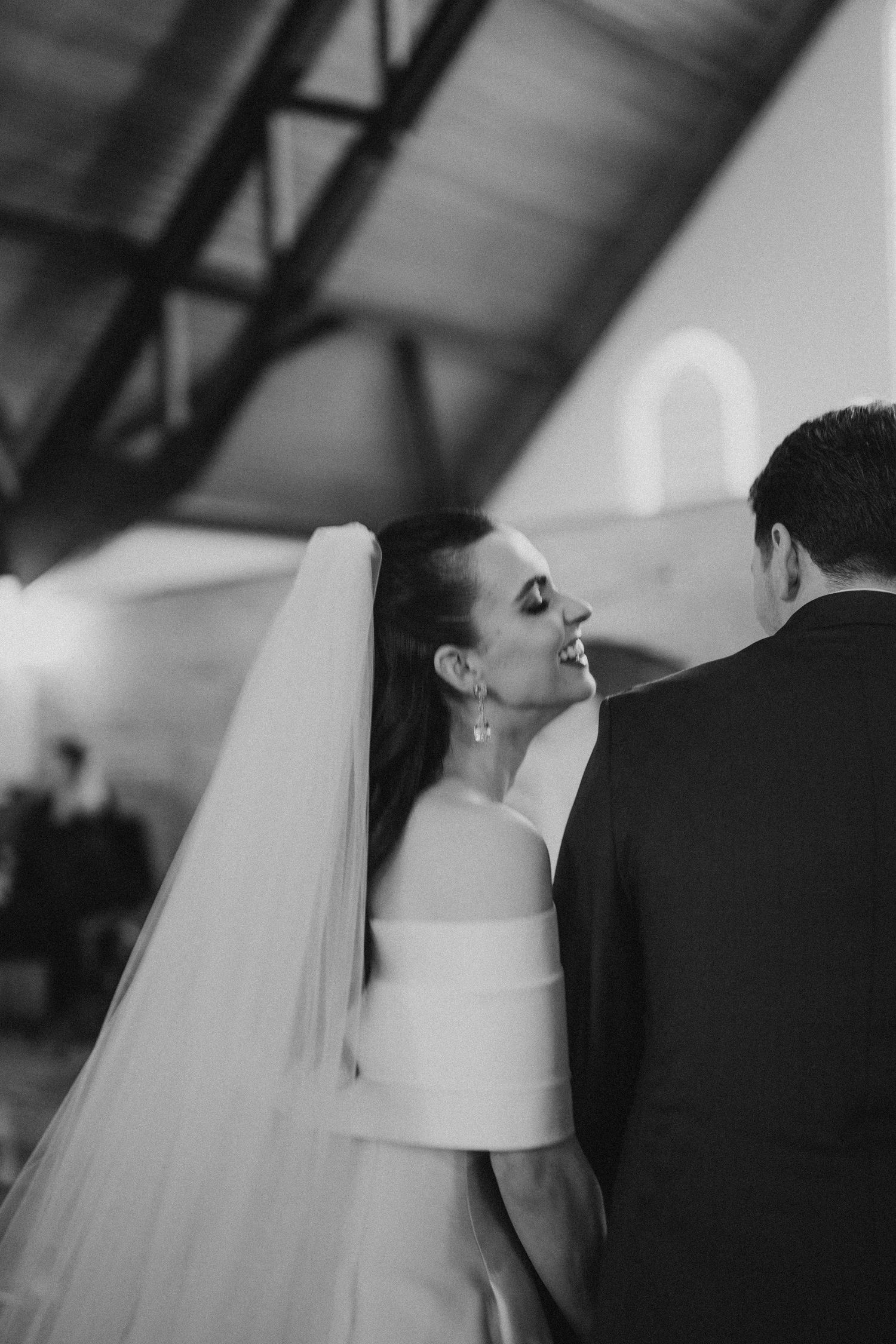 A black and white photo of a bride in a flowing veil during a wedding ceremony.