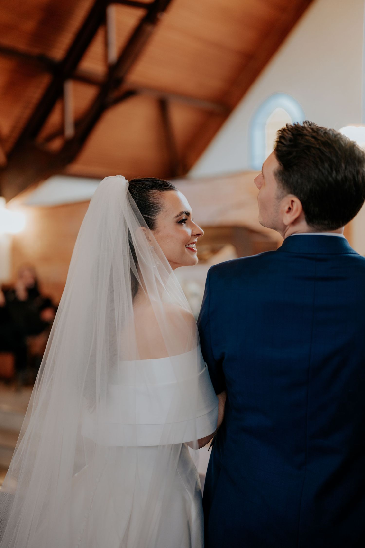 A bride in white dress and veil shares an intimate moment with her groom during the ceremony.