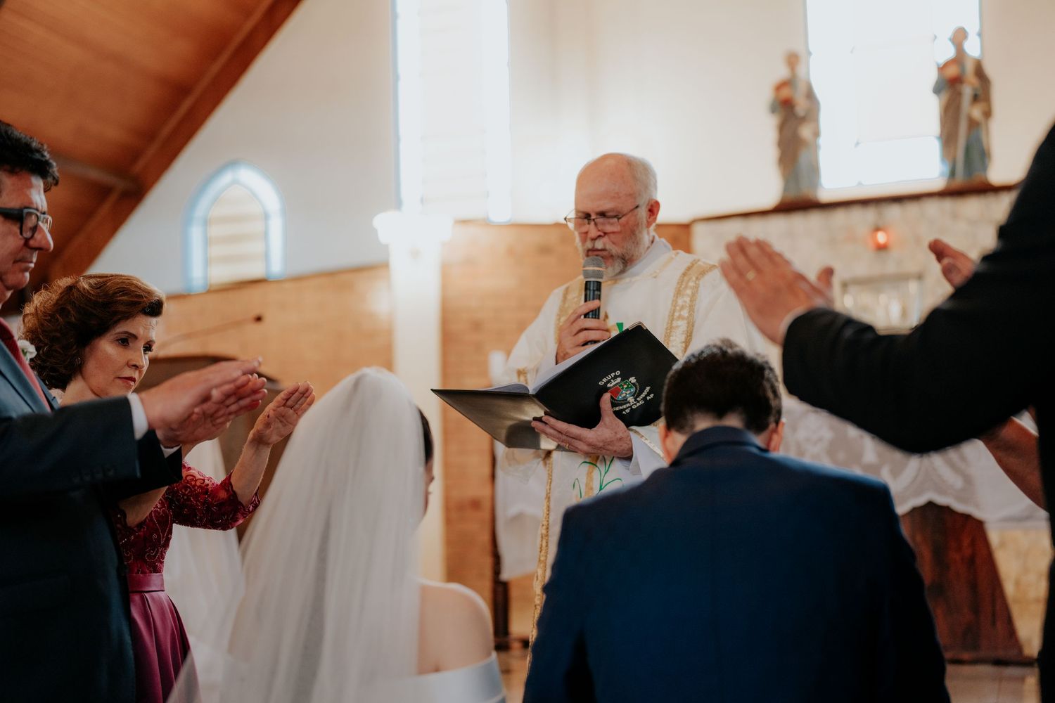 Wedding ceremony in progress inside a church with wooden walls and religious statues.