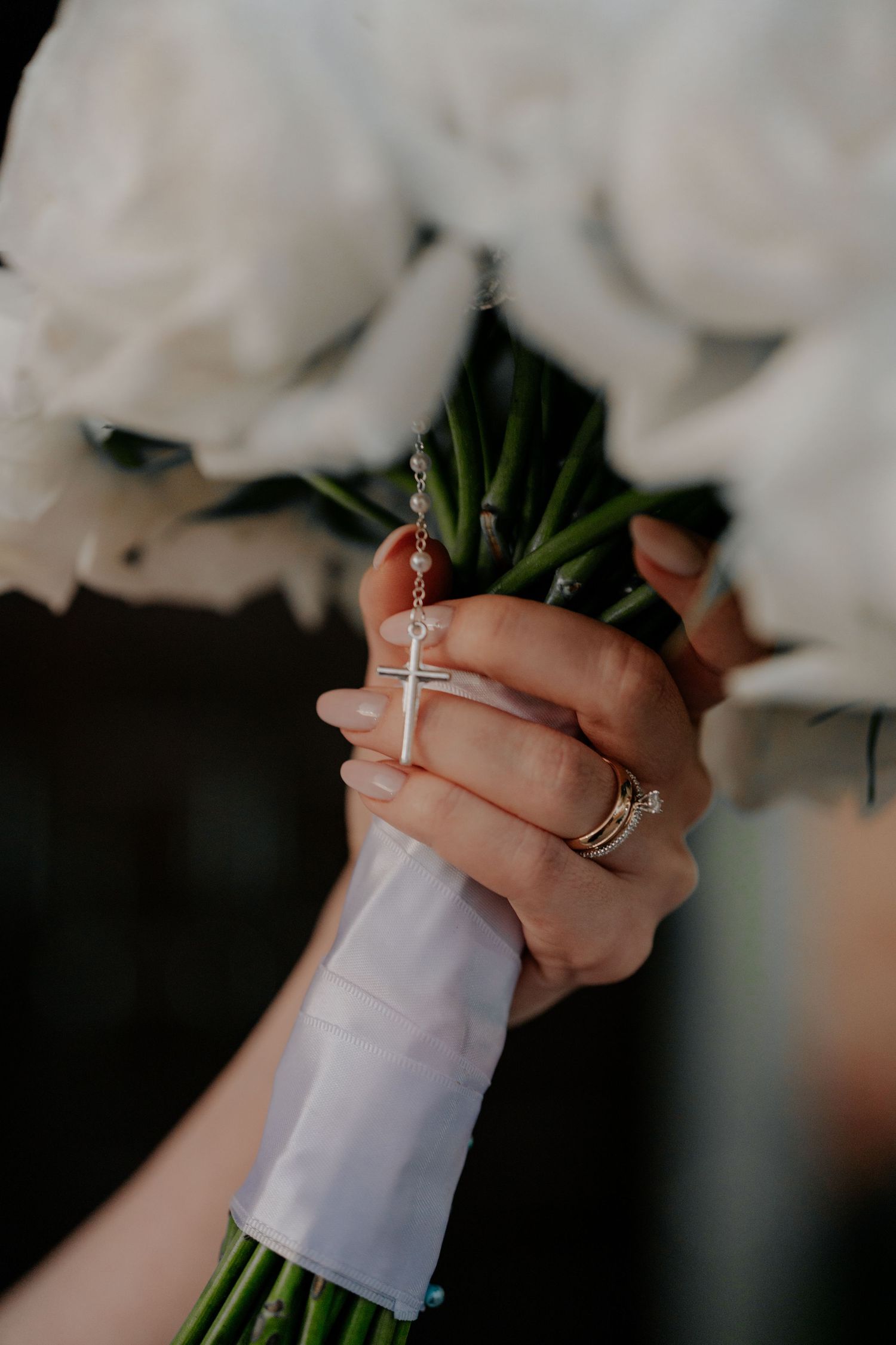Close-up of hands holding white bouquet with wedding rings visible.