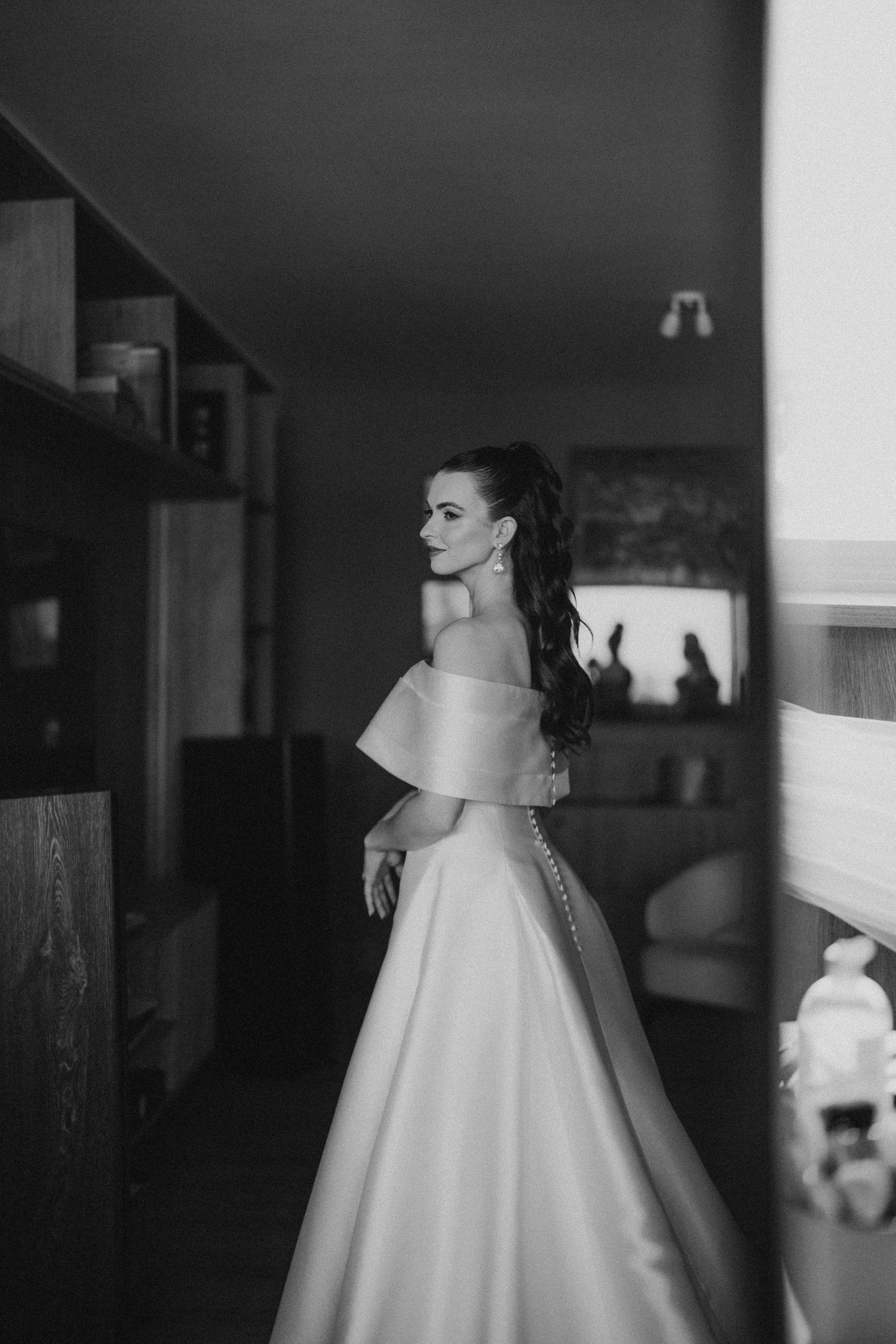 Elegant bride in off-shoulder gown poses in dramatic black and white silhouette.